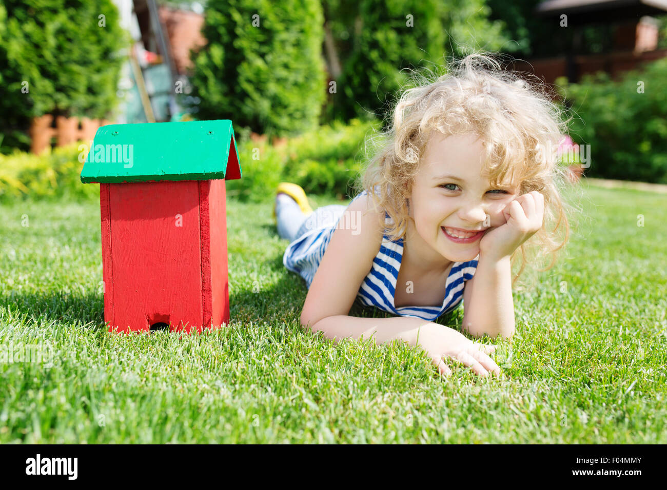 Modello in legno della casa e la bimba bionda giacente sul prato verde. Immobiliare di concetto Foto Stock