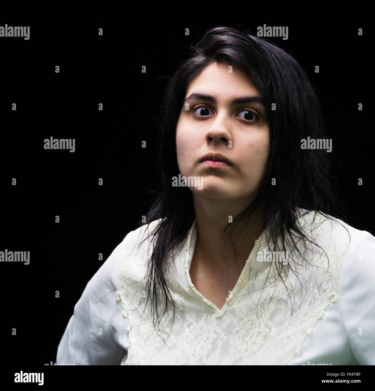 Latina adolescente in bianco in piedi di fronte a uno sfondo nero con un arrabbiato, sospetti gravi, irritato sguardo sul suo viso. Foto Stock