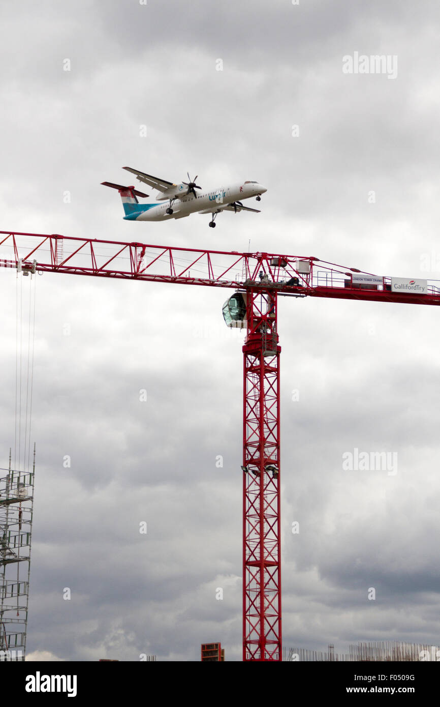 Luxair Bombardier Q400 twin a turboelica in atterraggio a City Airport London dietro di gru a torre galeoni a raggiungere lo sviluppo, Docklands Foto Stock
