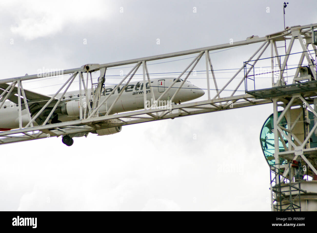 Helvetic Airways Embraer 190 in atterraggio a City Airport London dietro di gru a torre galeoni a raggiungere lo sviluppo, Docklands Foto Stock
