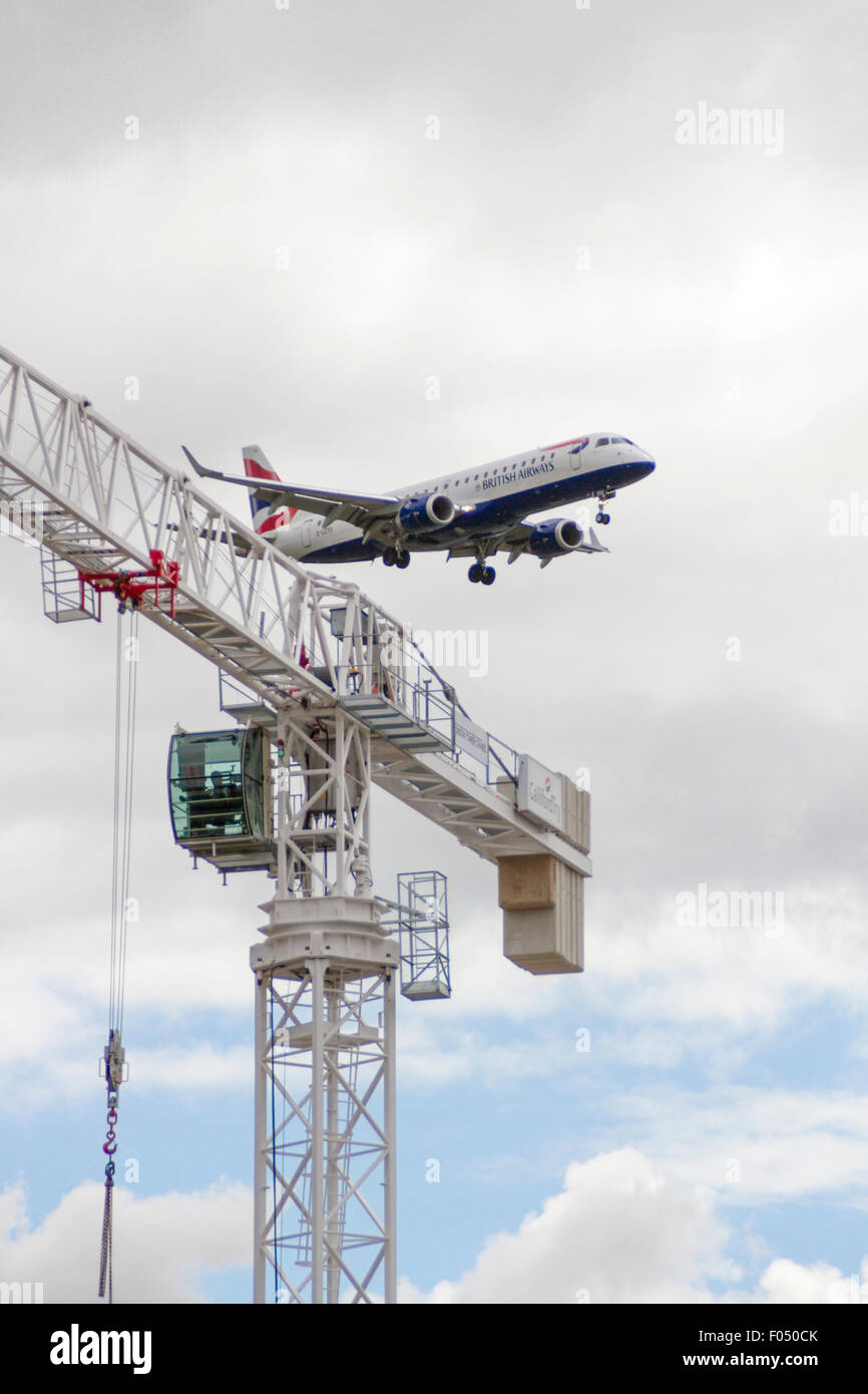 British Airways Airbus A318 in atterraggio a City Airport London dietro di gru a torre galeoni a raggiungere lo sviluppo, Docklands Foto Stock