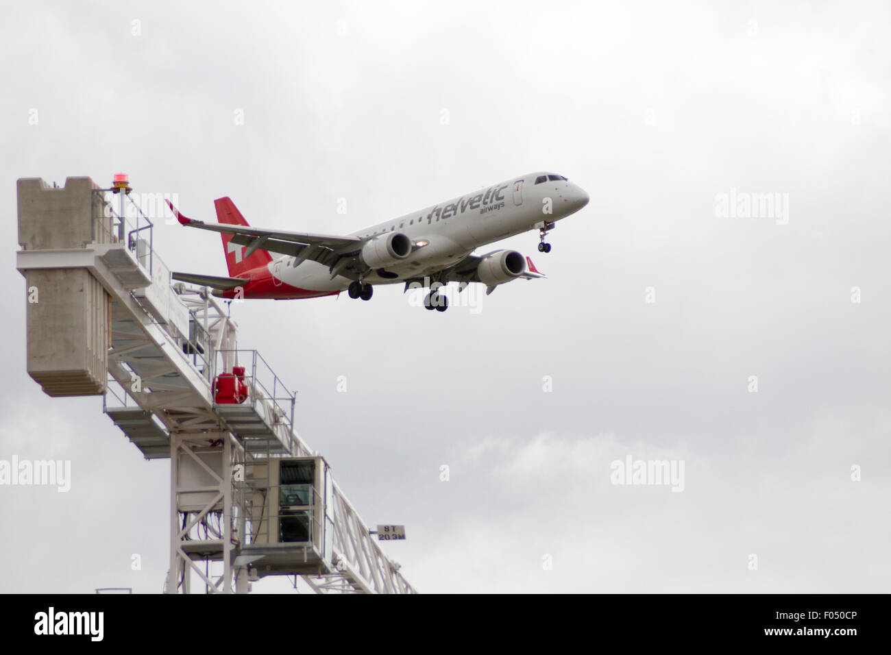 Helvetic Airways Embraer 190 in atterraggio a City Airport London dietro di gru a torre galeoni a raggiungere lo sviluppo, Docklands Foto Stock