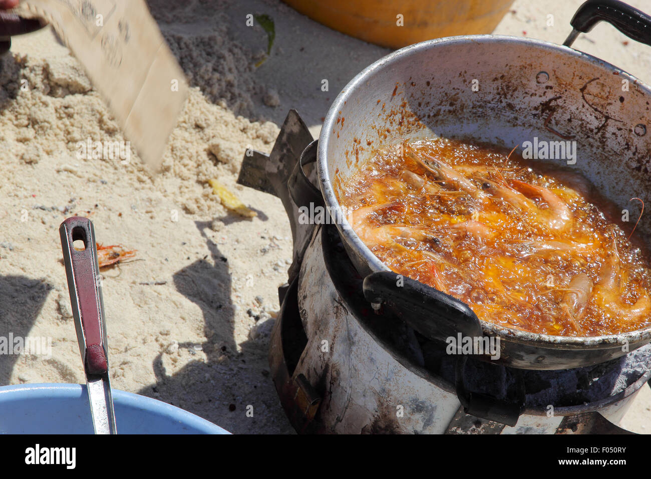 Una padella di olio caldo con gamberetti frittura sulla spiaggia con la sabbia come sfondo Foto Stock