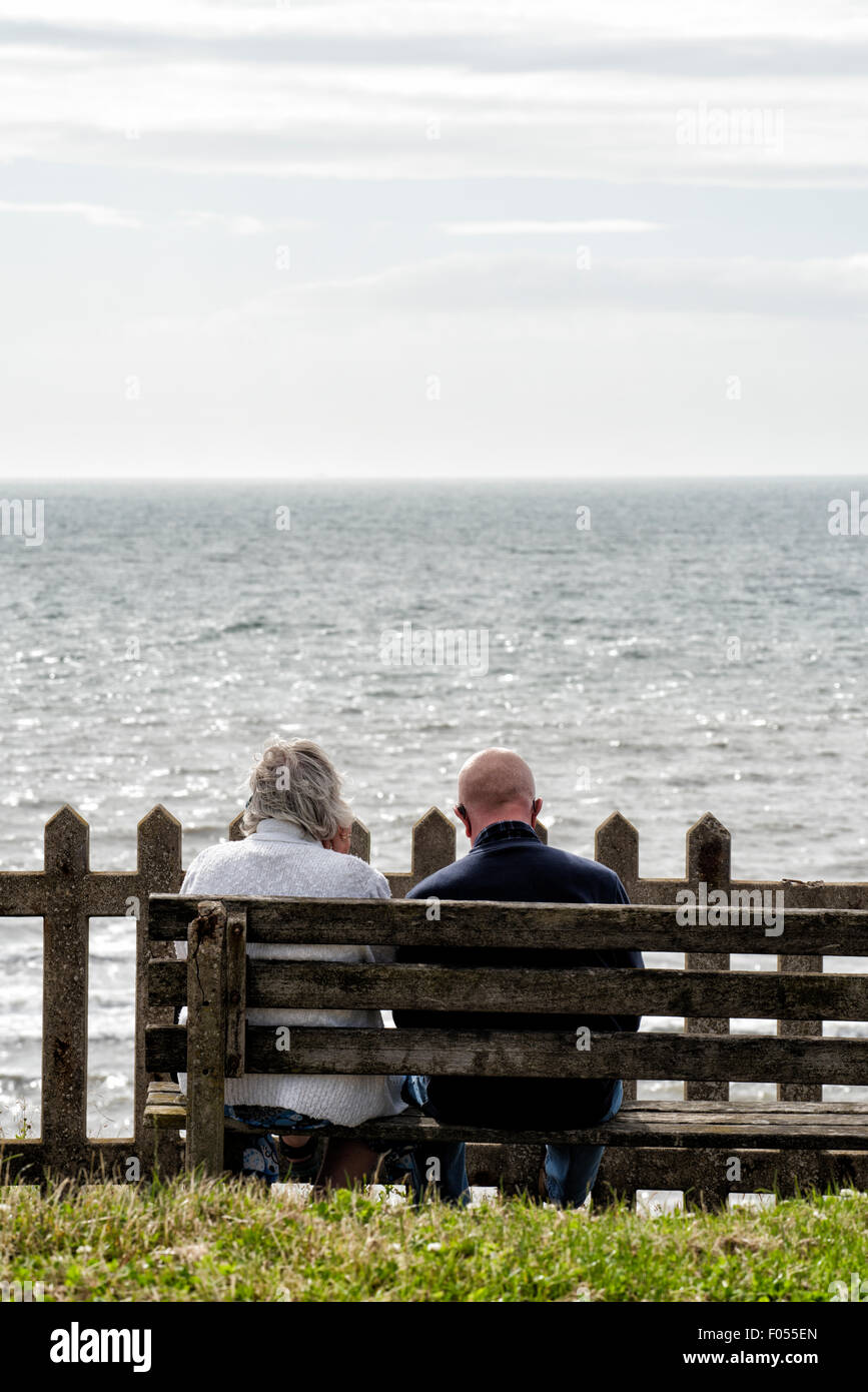 Coppia di anziani seduti sulla panca di legno di fronte al mare Foto Stock