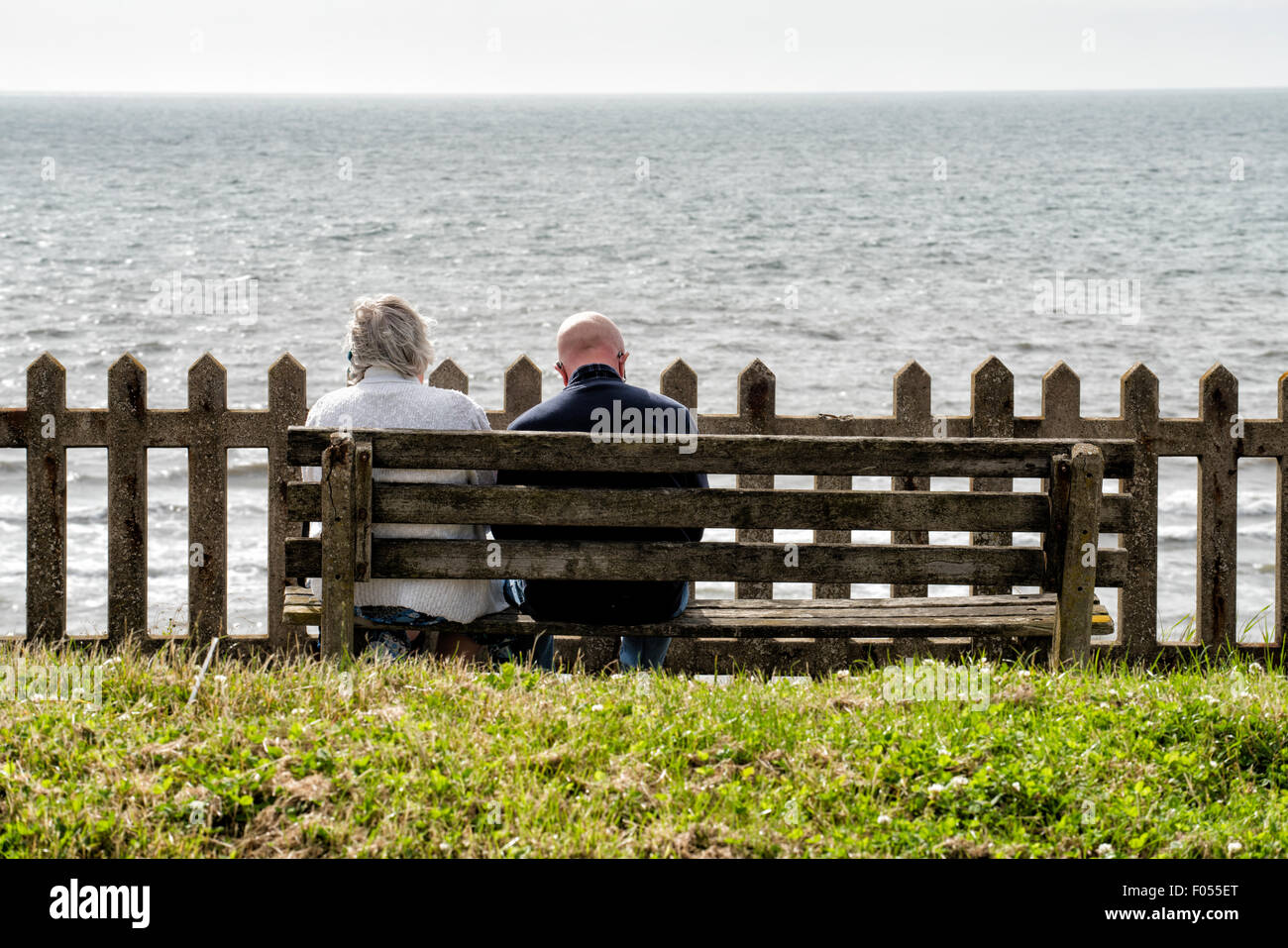 Coppia di anziani seduti sulla panca di legno di fronte al mare Foto Stock