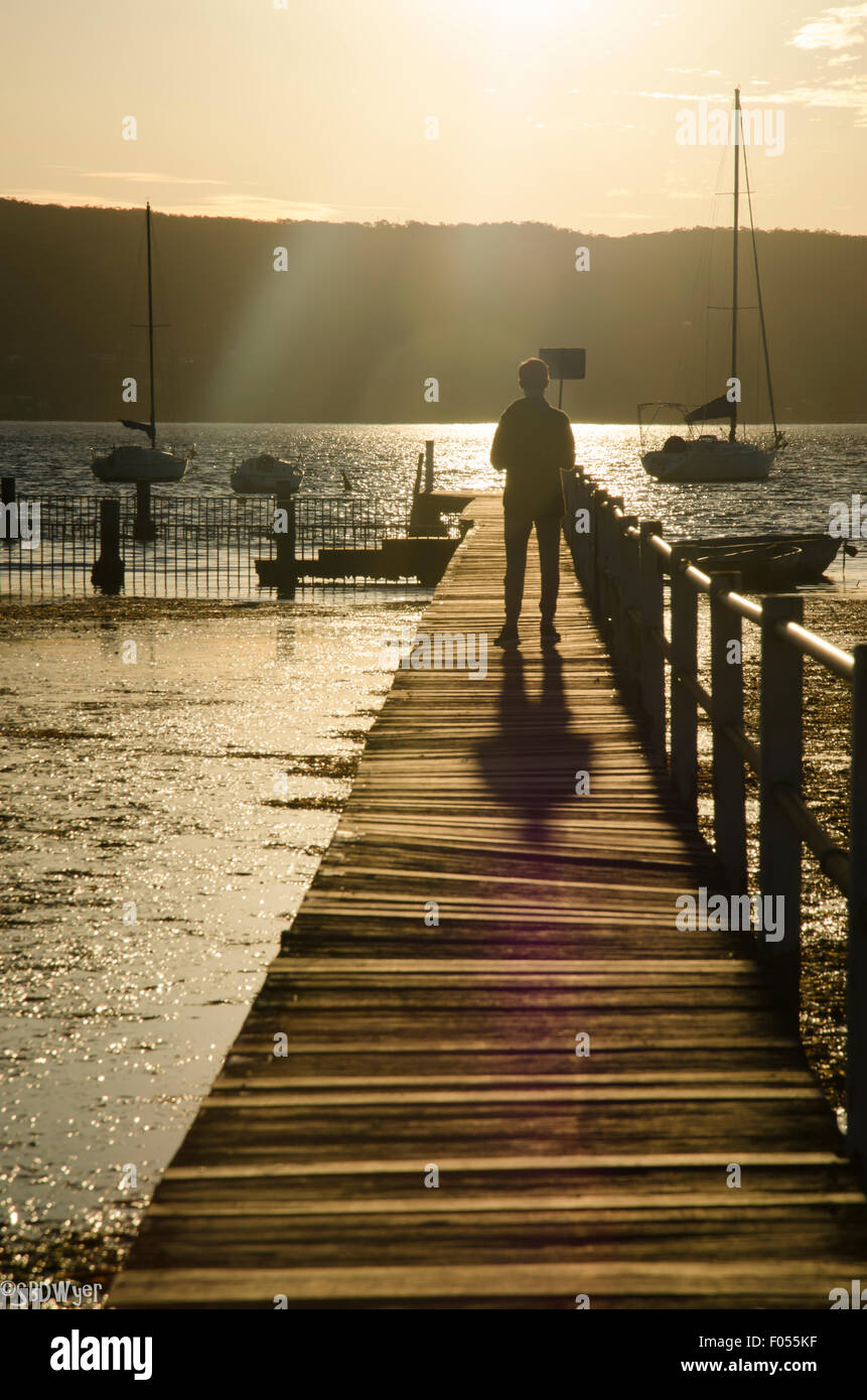 Un ragazzo (adolescente) camminando verso il tramonto su una stretta wharf Foto Stock