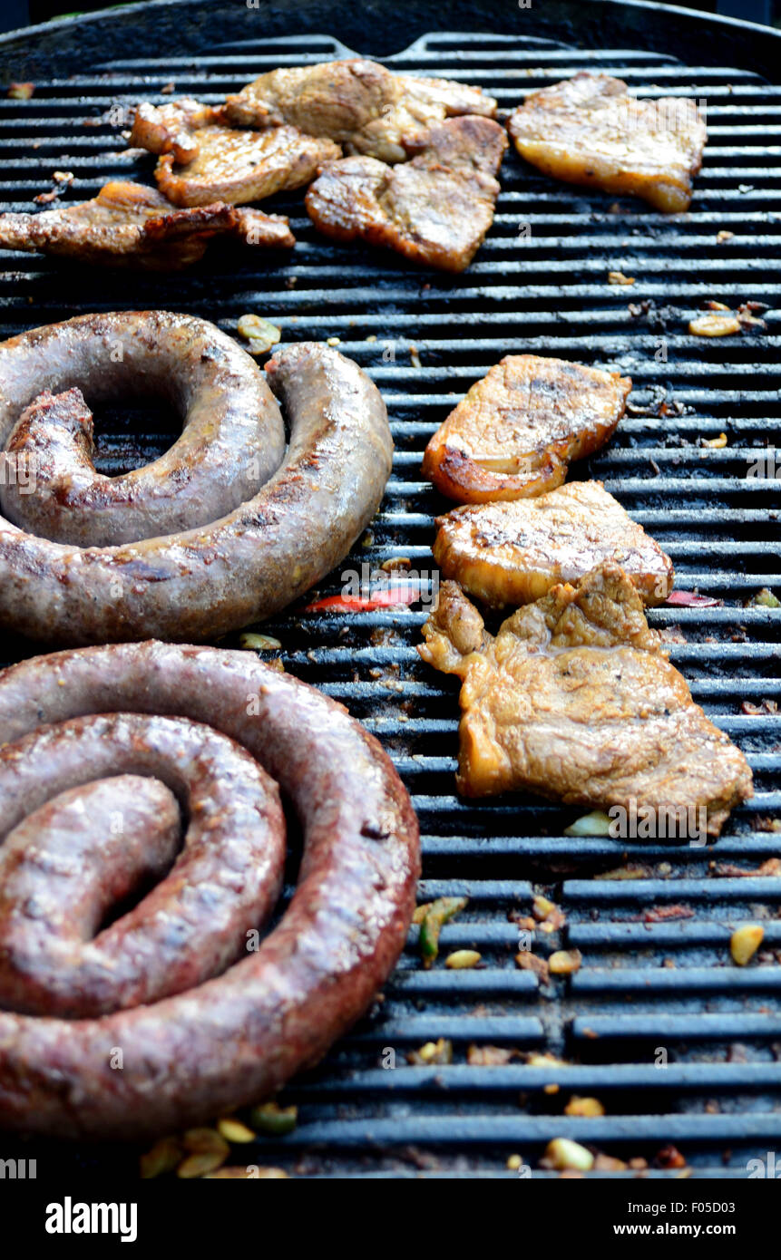 Salsicce e carne di maiale marinato la cottura su un barbecue. Foto Stock
