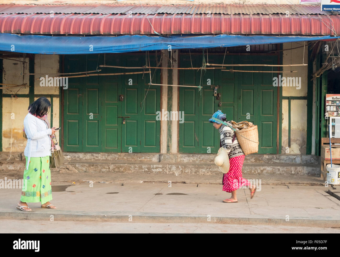 Città di Kalaw , Myanmar ( Birmania ) Una donna su un telefono cellulare e una donna che porta un cesto Foto Stock