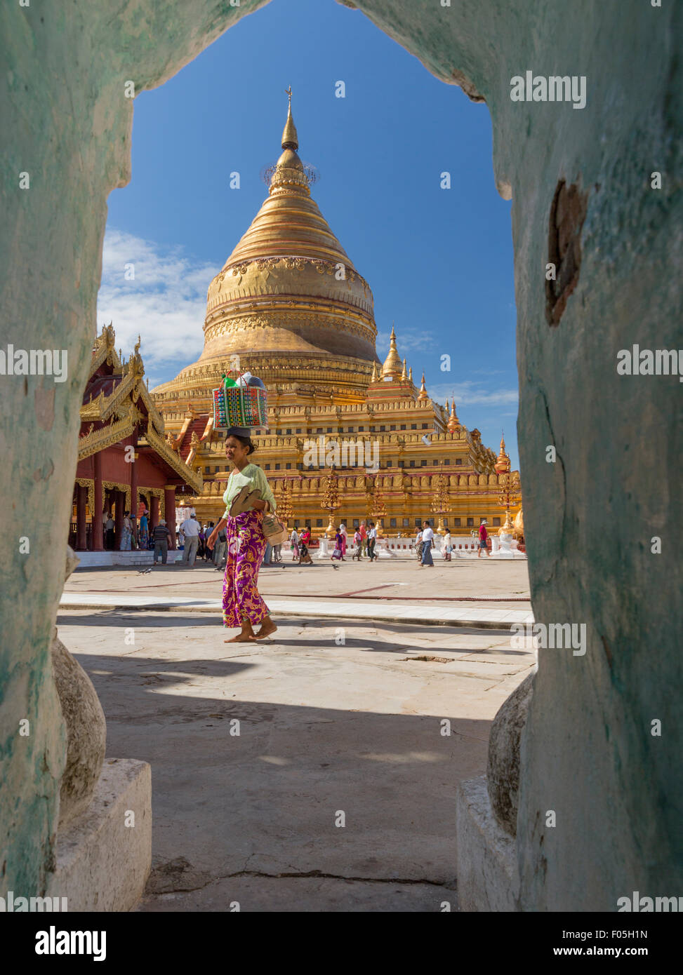 Donna cestello porta sul suo capo passeggiate tra Plaza di fronte alla Pagoda Shwezigon stupa in Nyaung U Myanmar. Vista inquadrato in arch Foto Stock