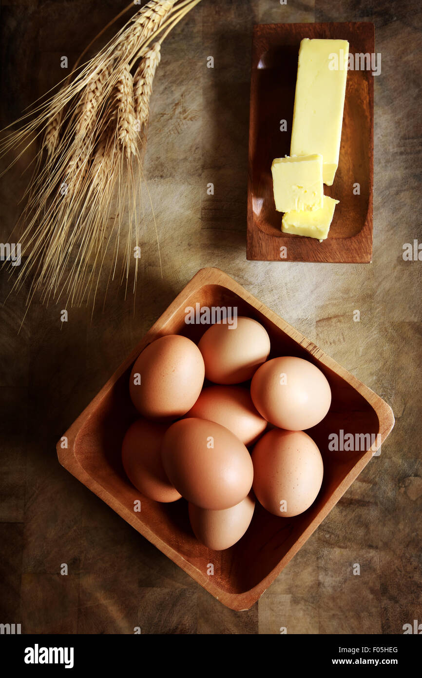 Uova con burro e grano su tavola in legno rustico Foto Stock