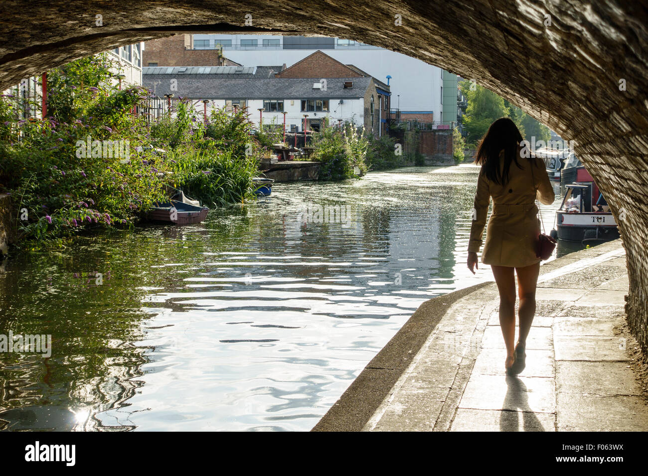 Giovane donna cammina verso la luce sotto un ponte da un canale nella zona est di Londra, Regno Unito. Foto Stock