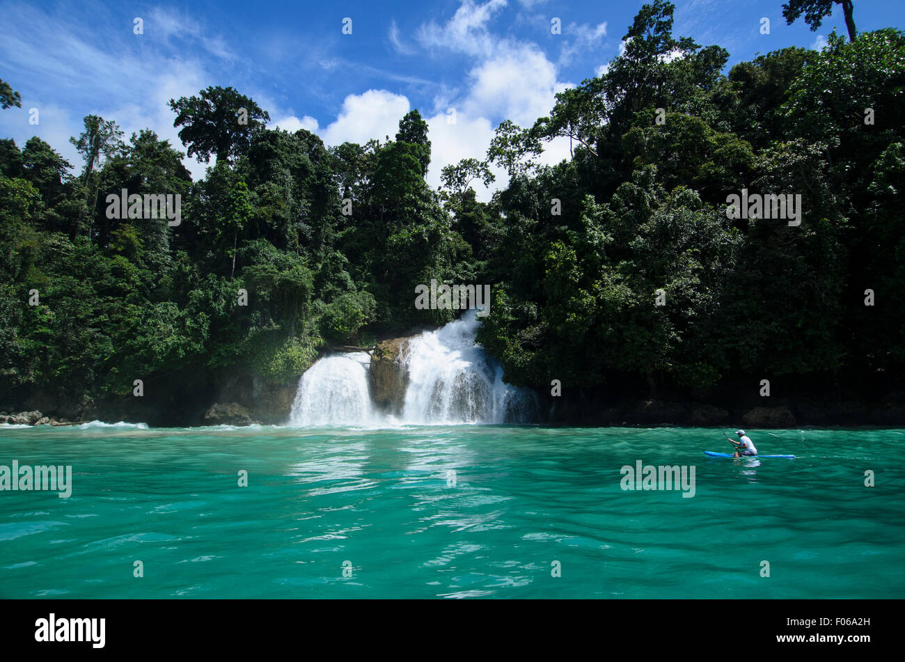 Un kayaker pagaie passato una cascata crollate nell'oceano, Mommon, Banda Mare, West Papua provincia, Indonesia, Oceano Pacifico Foto Stock