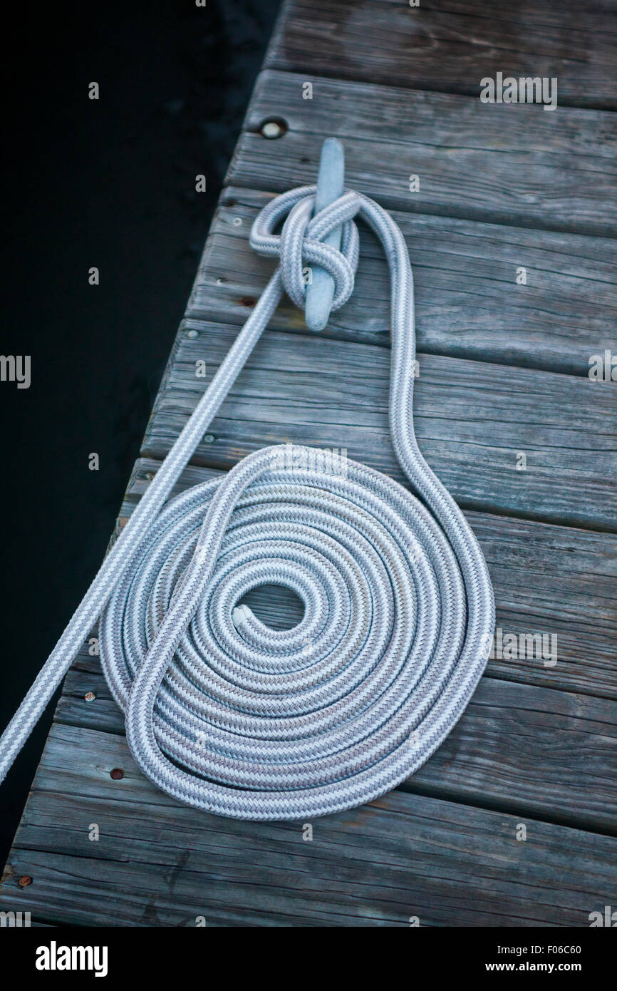 Linea di barca legata a un dock a gancio che è avvolto ordinatamente sulla cima di un dock in legno Foto Stock