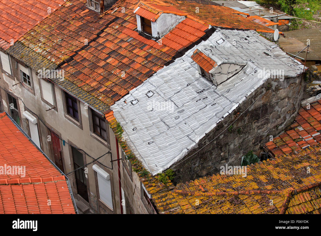 Case tradizionali con tetti di tegole rosse, uno di essi coperto con un foglio di alluminio isolamento Foto Stock