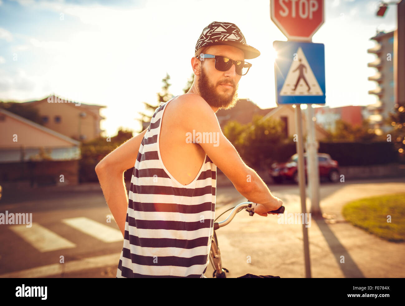 Giovane uomo elegante in occhiali da sole di una bicicletta su una strada di città alla luce del tramonto Foto Stock