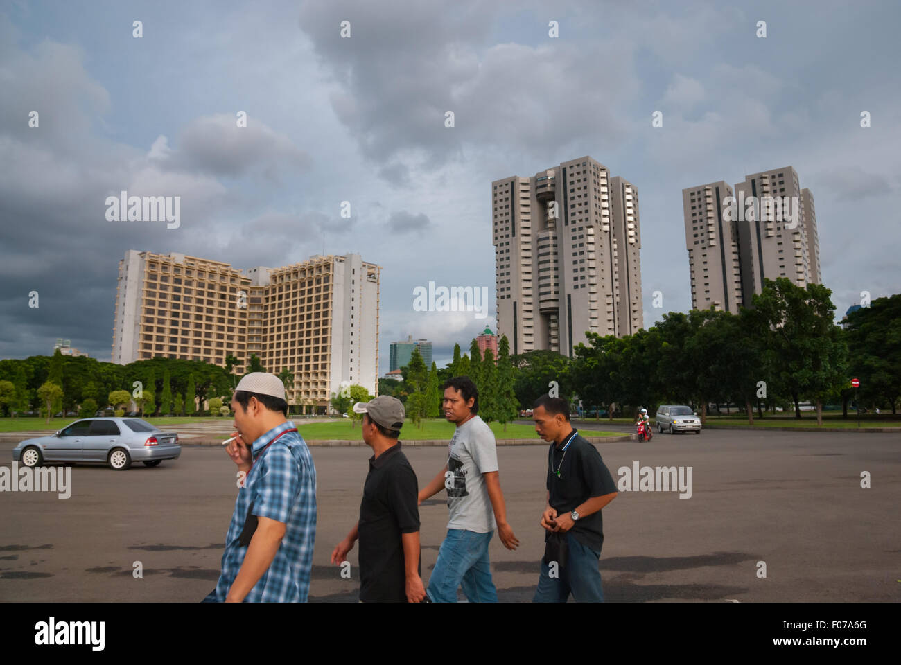 Giacarta: Un gruppo di uomini che camminano su una strada intorno al parco est in Gelora Bung Karno (complesso sportivo Senayan) con edifici torreggianti in lontananza. Foto Stock