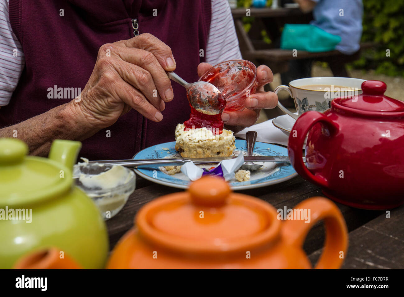 Donna titolare di pensione o di rendita mettendo jam su scone presso il cafe con vasi di tè Foto Stock