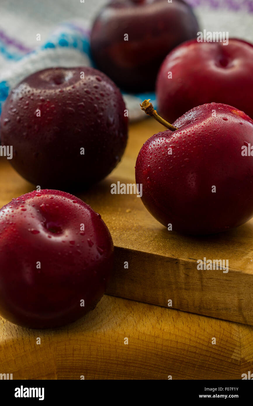 Cinque Neri freschi di prugne di diamante su tavole di legno. Bagnare con gocce d'acqua. Il cibo ancora in vita. Messa a fuoco selettiva. Back lit. Foto Stock