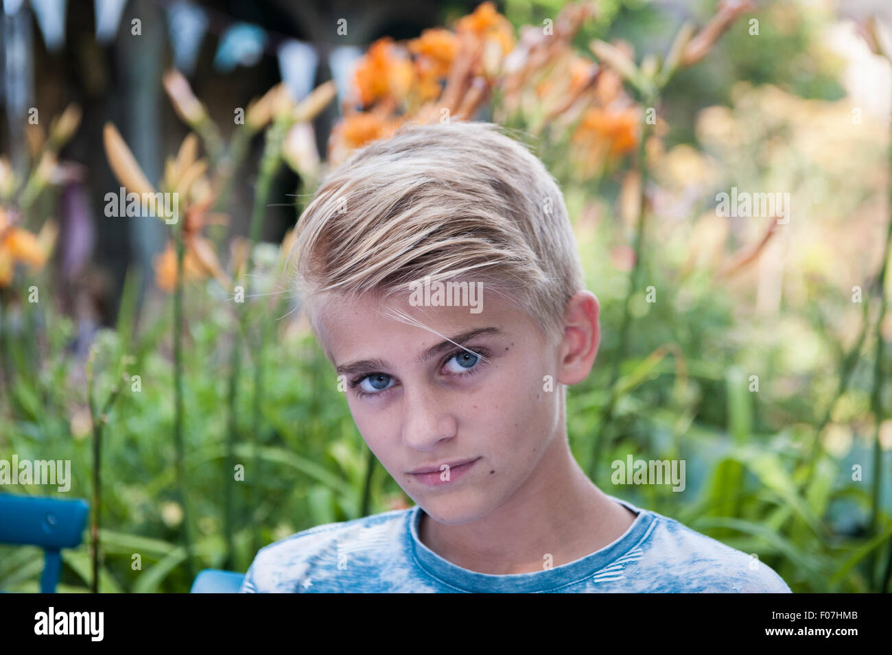Guardare un buon ragazzo biondo guarda nella telecamera in un paese inglese giardino con piante e pavese in background Foto Stock