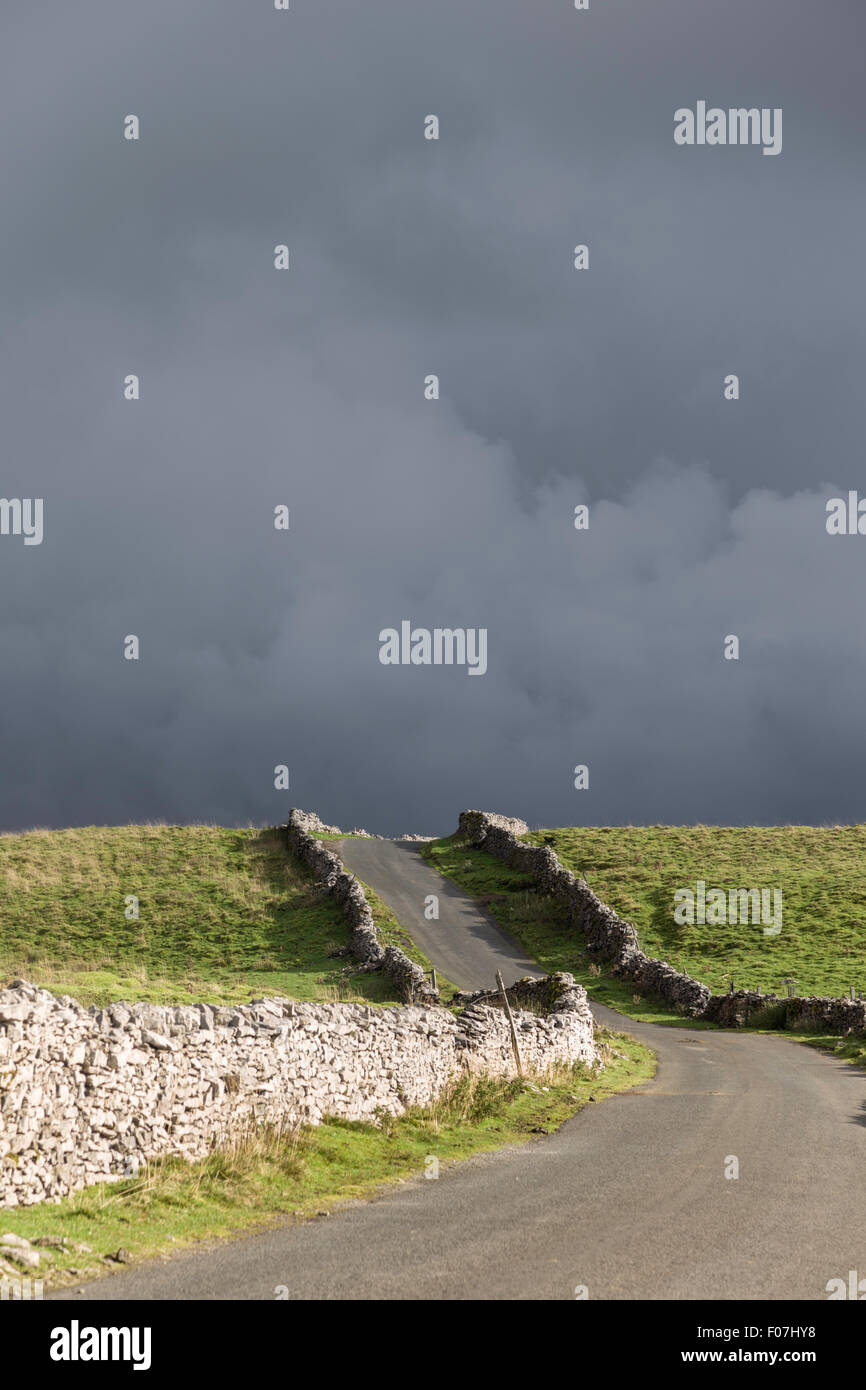 Nuvole temporalesche oltre il fells su un altopiano di strada di campagna, Yorkshire Dales National Park, England, Regno Unito Foto Stock