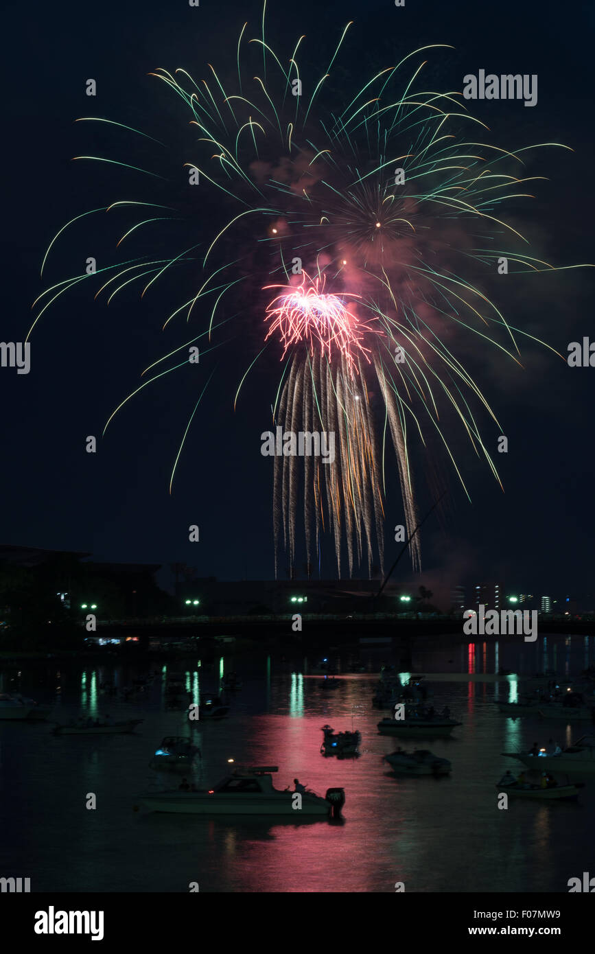 Coloratissimi fuochi d'artificio riflessa in un fiume con molte piccole barche e un paesaggio urbano lungo il fianco nella campagna di Kochi, Giappone. Foto Stock