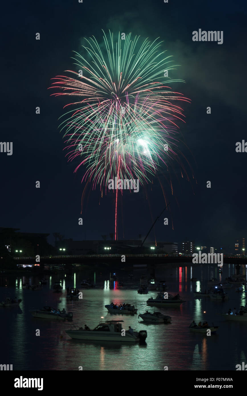 Coloratissimi fuochi d'artificio riflessa in un fiume con molte piccole barche e un paesaggio urbano lungo il fianco nella campagna di Kochi, Giappone. Foto Stock