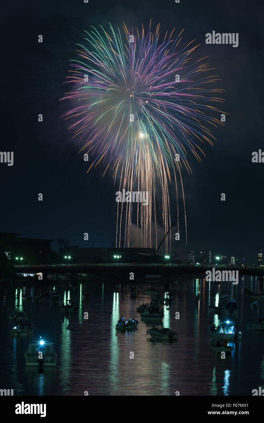 Coloratissimi fuochi d'artificio riflessa in un fiume con molte piccole barche e un paesaggio urbano lungo il fianco nella campagna di Kochi, Giappone. Foto Stock