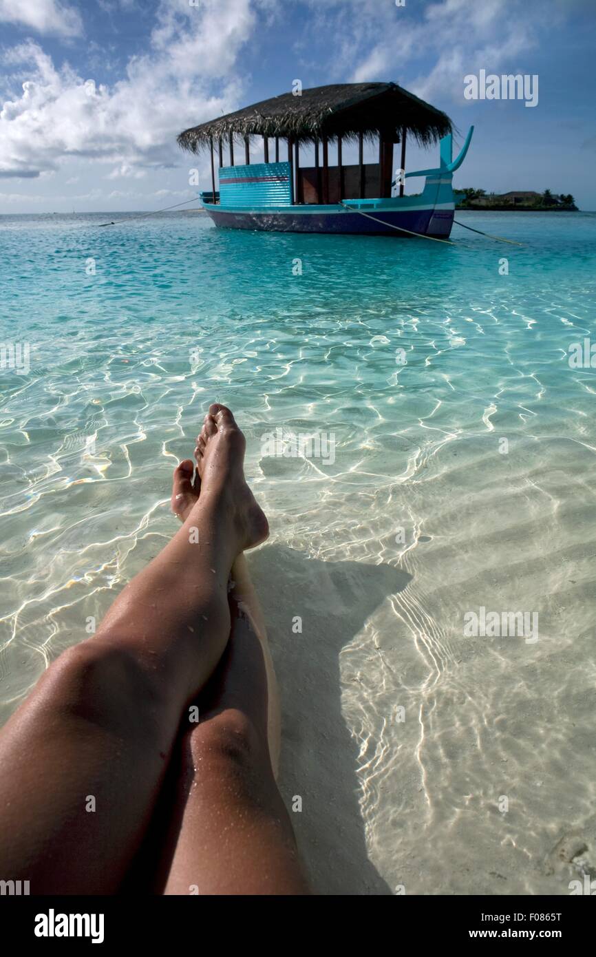 Close-up di gambe in acque poco profonde e barca in Veliganduhuraa isola, Maldive Foto Stock