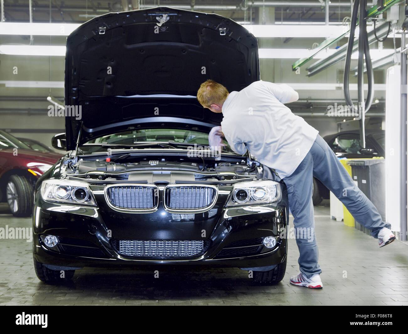 Il tecnico cerca all'interno del vano motore di auto in BMW World, Monaco di Baviera, Germania Foto Stock