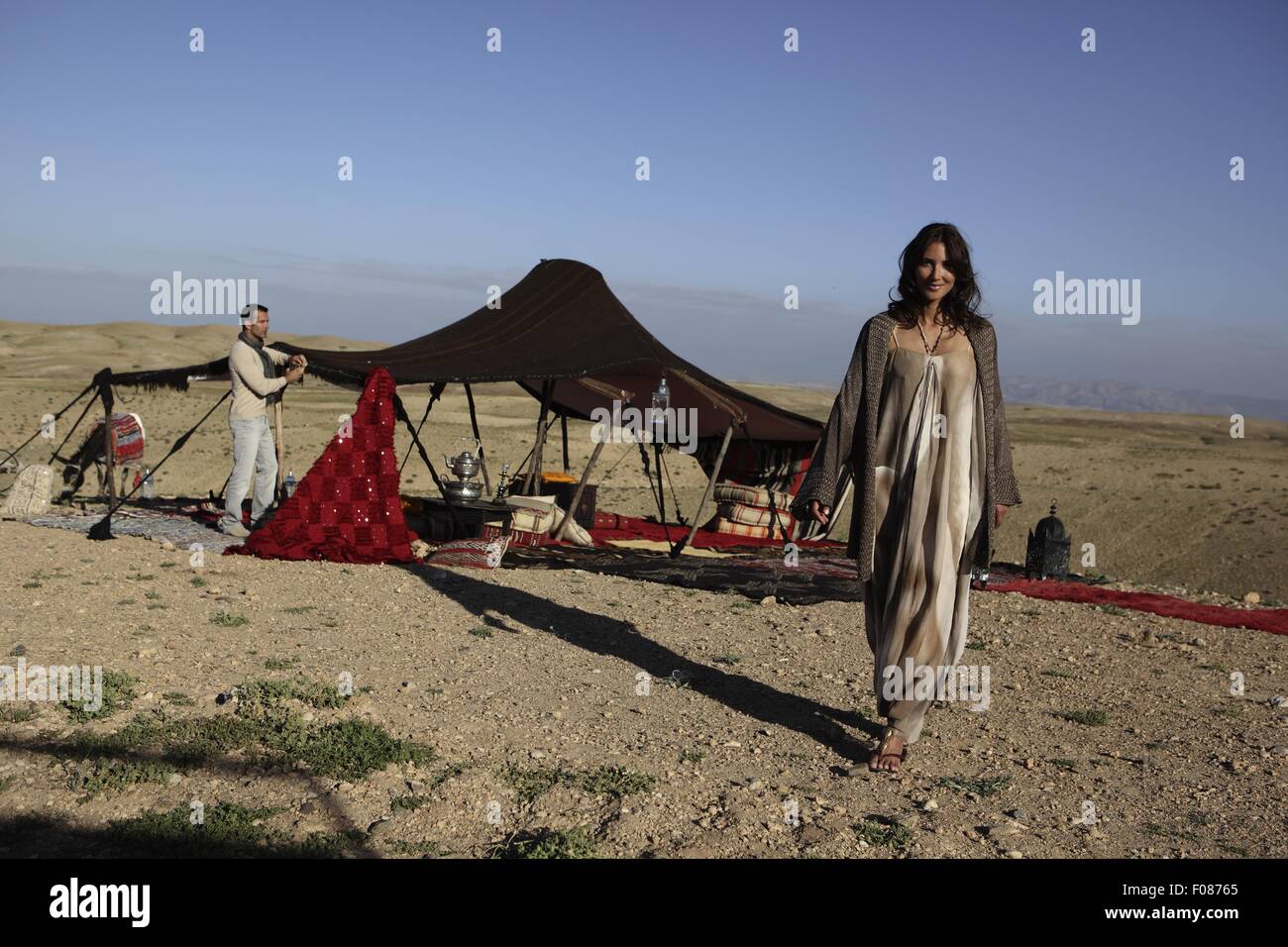 Donna che indossa lungo abito orientale a piedi mentre l'uomo costruire  tenda nel deserto Foto stock - Alamy