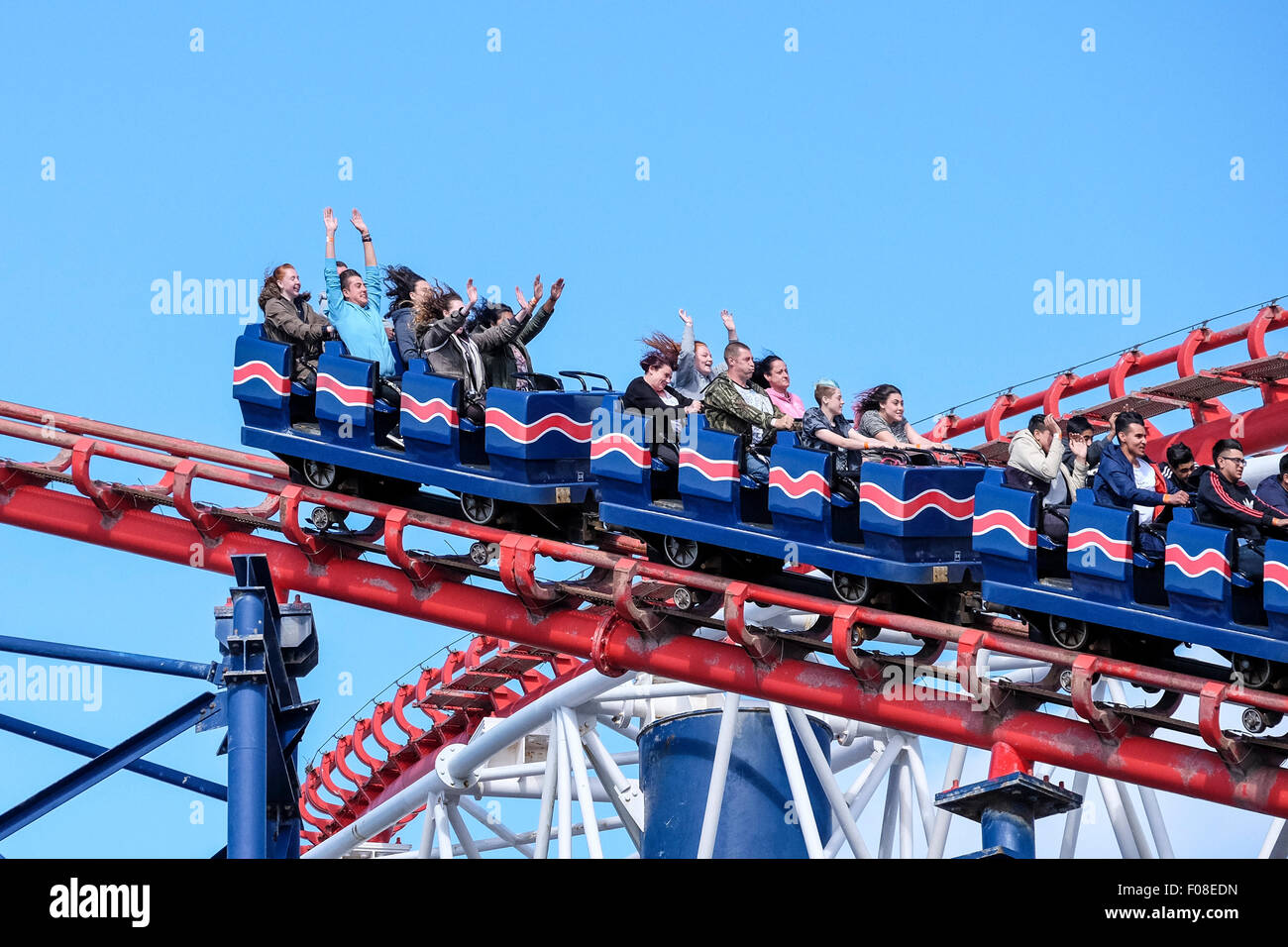 La gente a cavallo dei Big One a Blackpool Pleasure Beach con le loro mani detenute aloft su una giornata estiva con cielo blu. Foto Stock