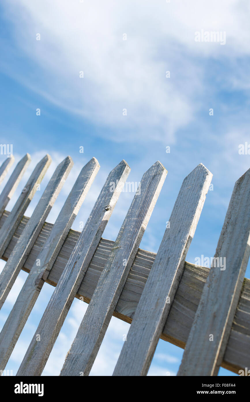 Basso angolo di visione, di un vecchio di legno Picket Fence, contro un cielo blu con nuvole. Foto Stock