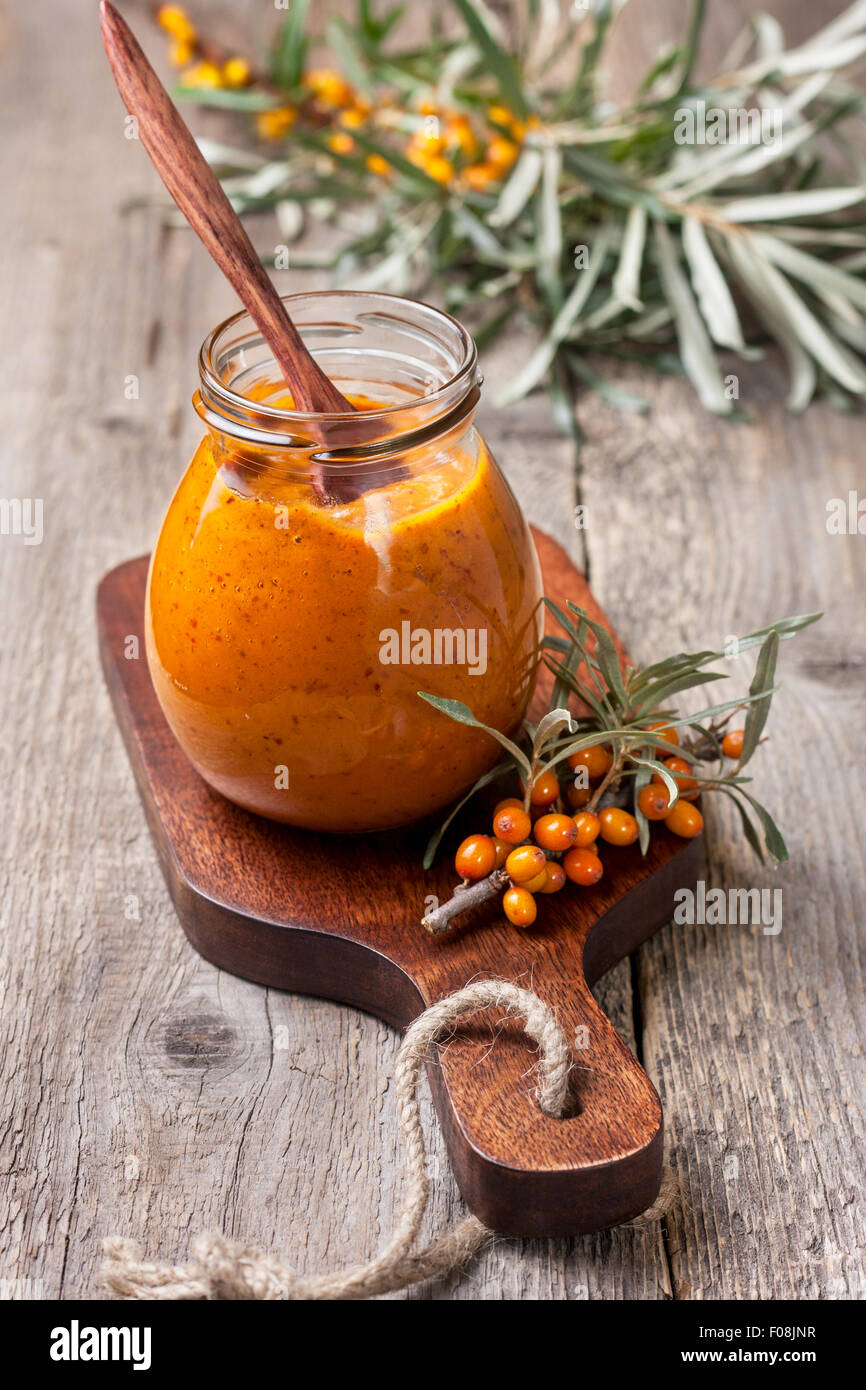 Vaso di vetro con bacche di olivello spinoso jam su uno sfondo di legno Foto Stock
