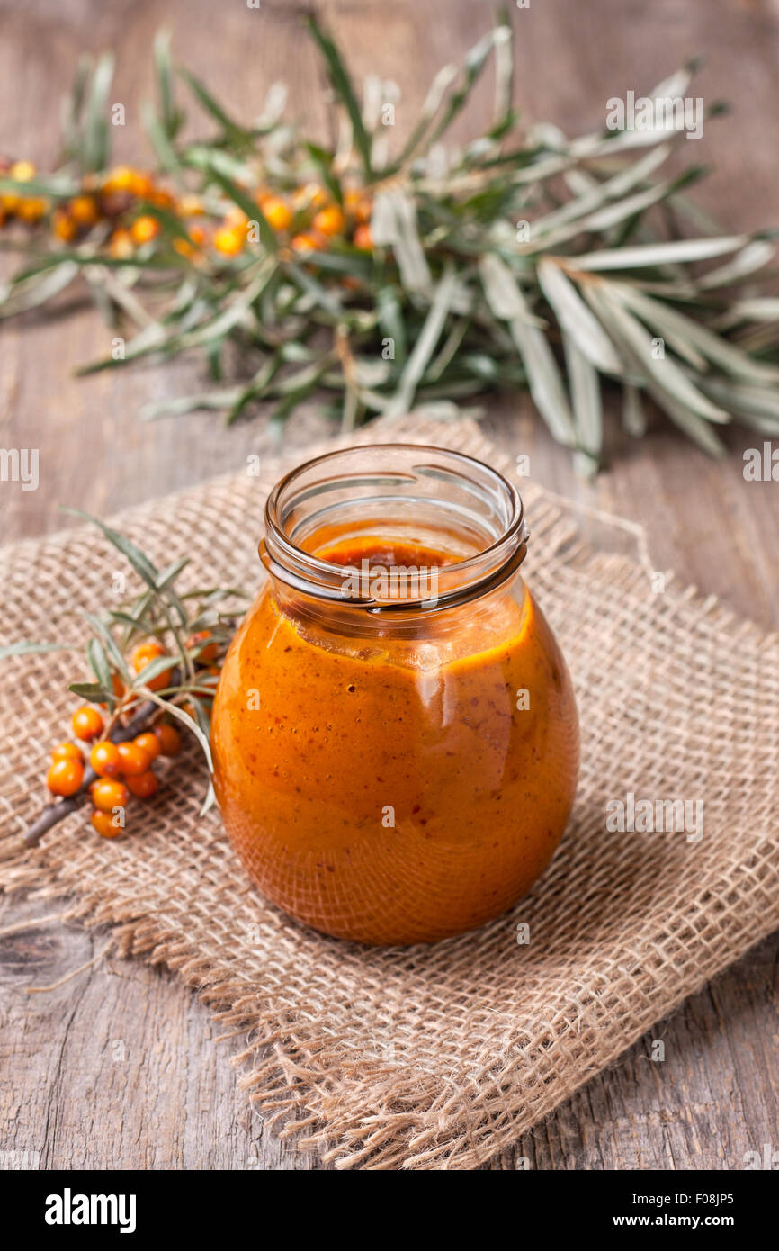 Vaso di vetro con bacche di olivello spinoso jam su uno sfondo di legno Foto Stock