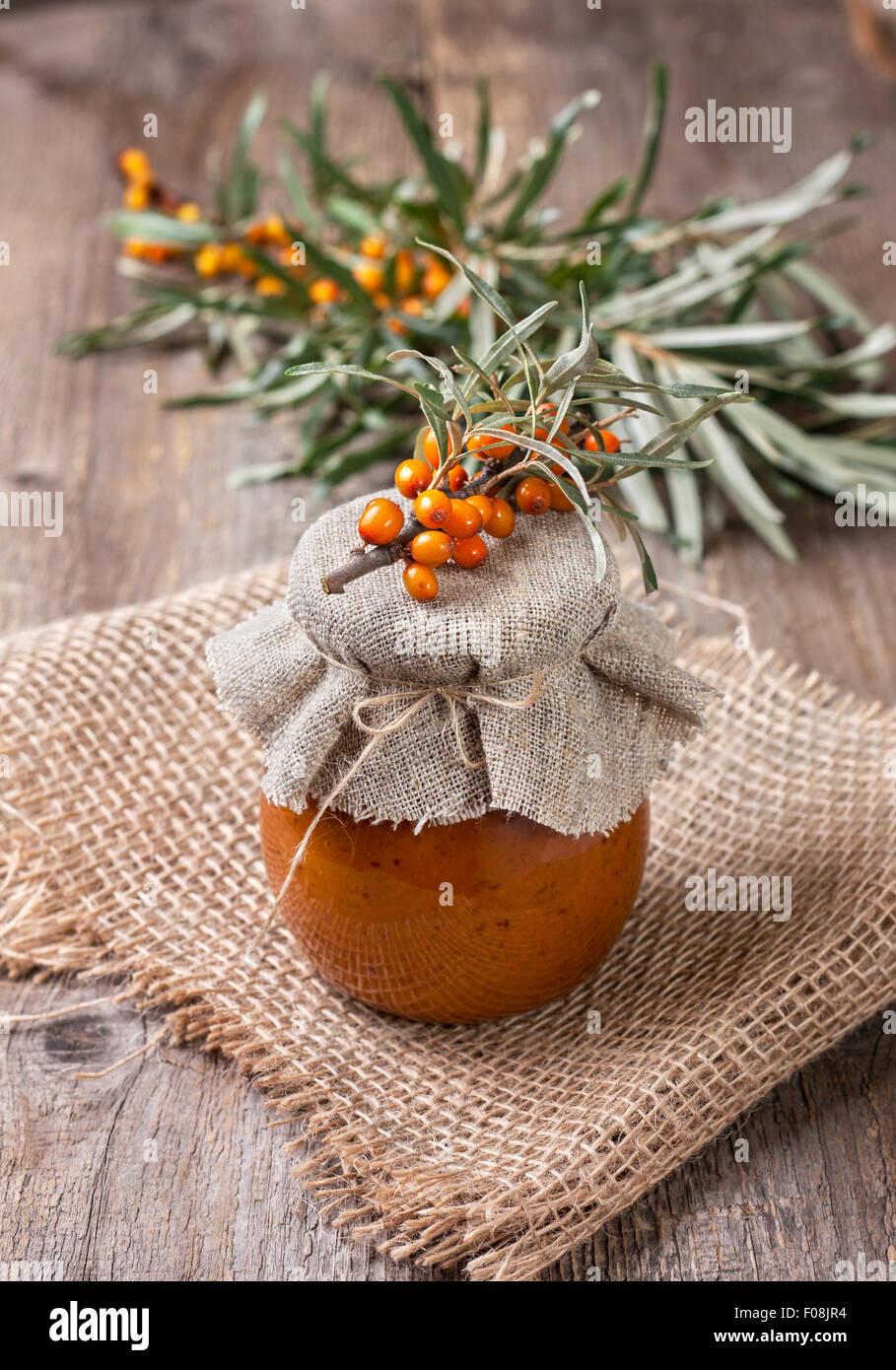 Vaso di vetro con bacche di olivello spinoso jam su uno sfondo di legno Foto Stock