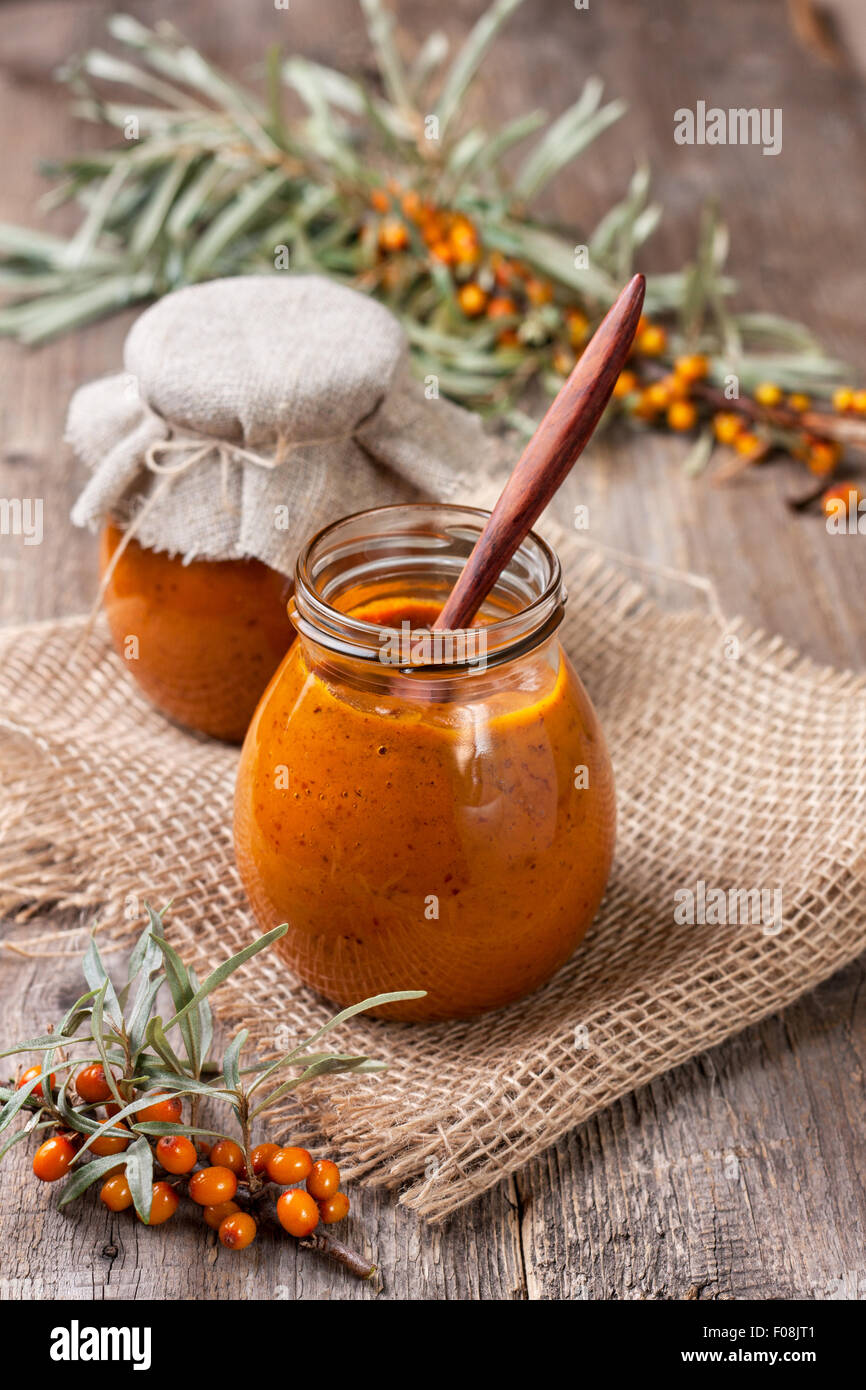 Vaso di vetro con bacche di olivello spinoso jam su uno sfondo di legno Foto Stock