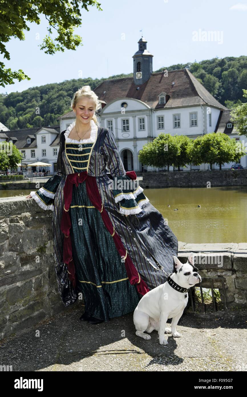 Donna vestita tradizionalmente in piedi a Bad Karl harbour con il cane, Huguenot, Hesse, Germania Foto Stock
