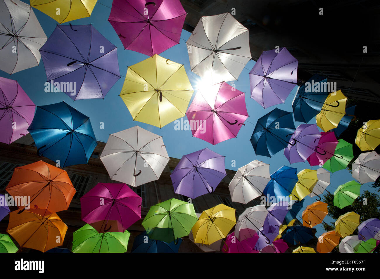 Vivacemente colorato floating ombrelloni riempire il cielo sopra la Rue Jean Jaures, Arles,Bouches-du-Rhône, Provenza, Francia Foto Stock