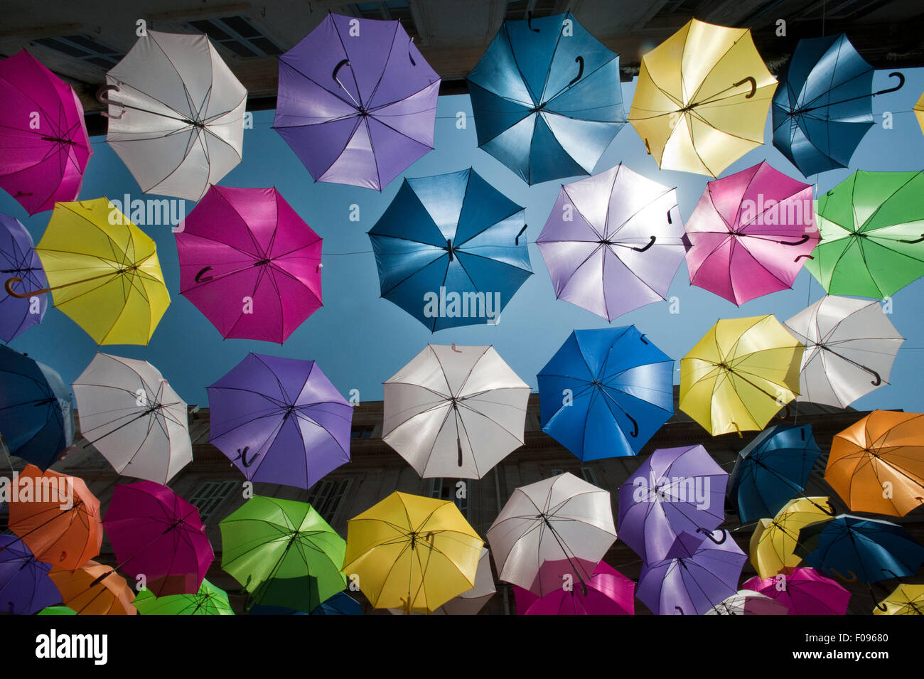 Vivacemente colorato floating ombrelloni riempire il cielo sopra la Rue Jean Jaures, Arles,Bouches-du-Rhône, Provenza, Francia Foto Stock