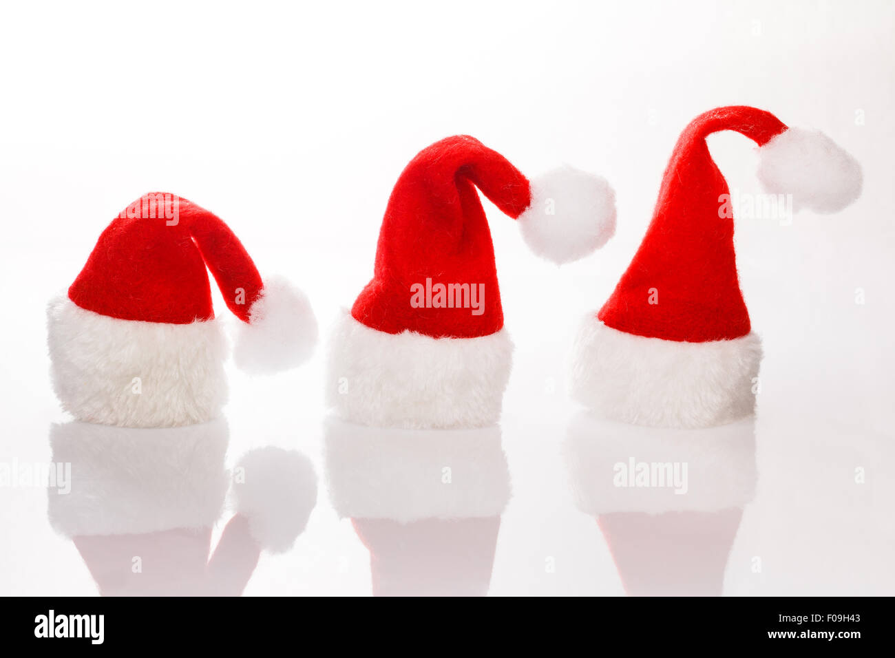 Tre cappelli Santa in una fila per il Natale. Isolato su sfondo bianco con la riflessione. Spazio per testo, copiare lo spazio. Foto Stock