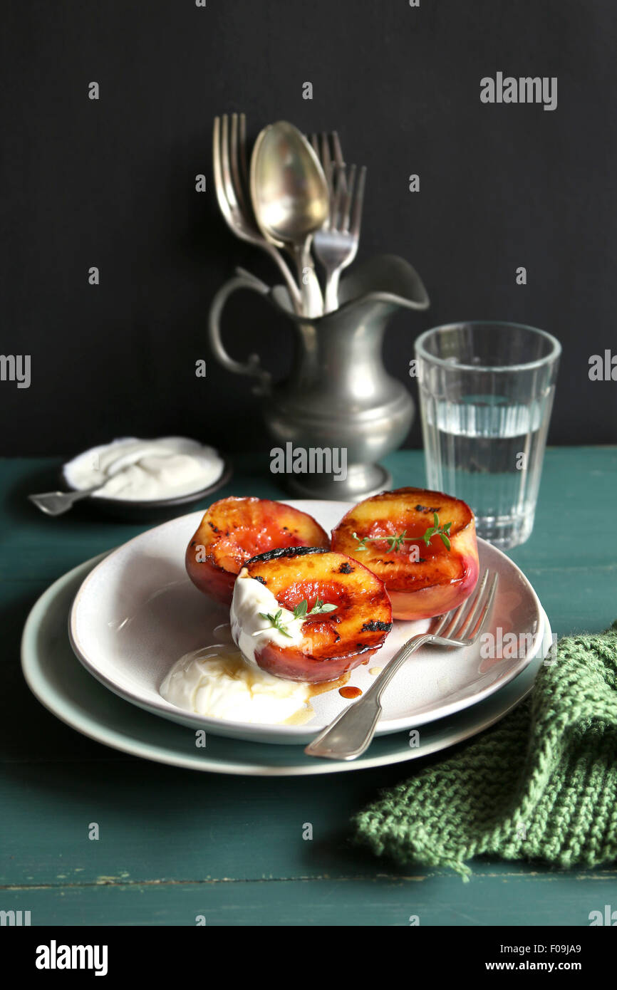 Piastra con grigliate di pesche con lo yogurt greco e miele e decorate con di timo fresco Foto Stock