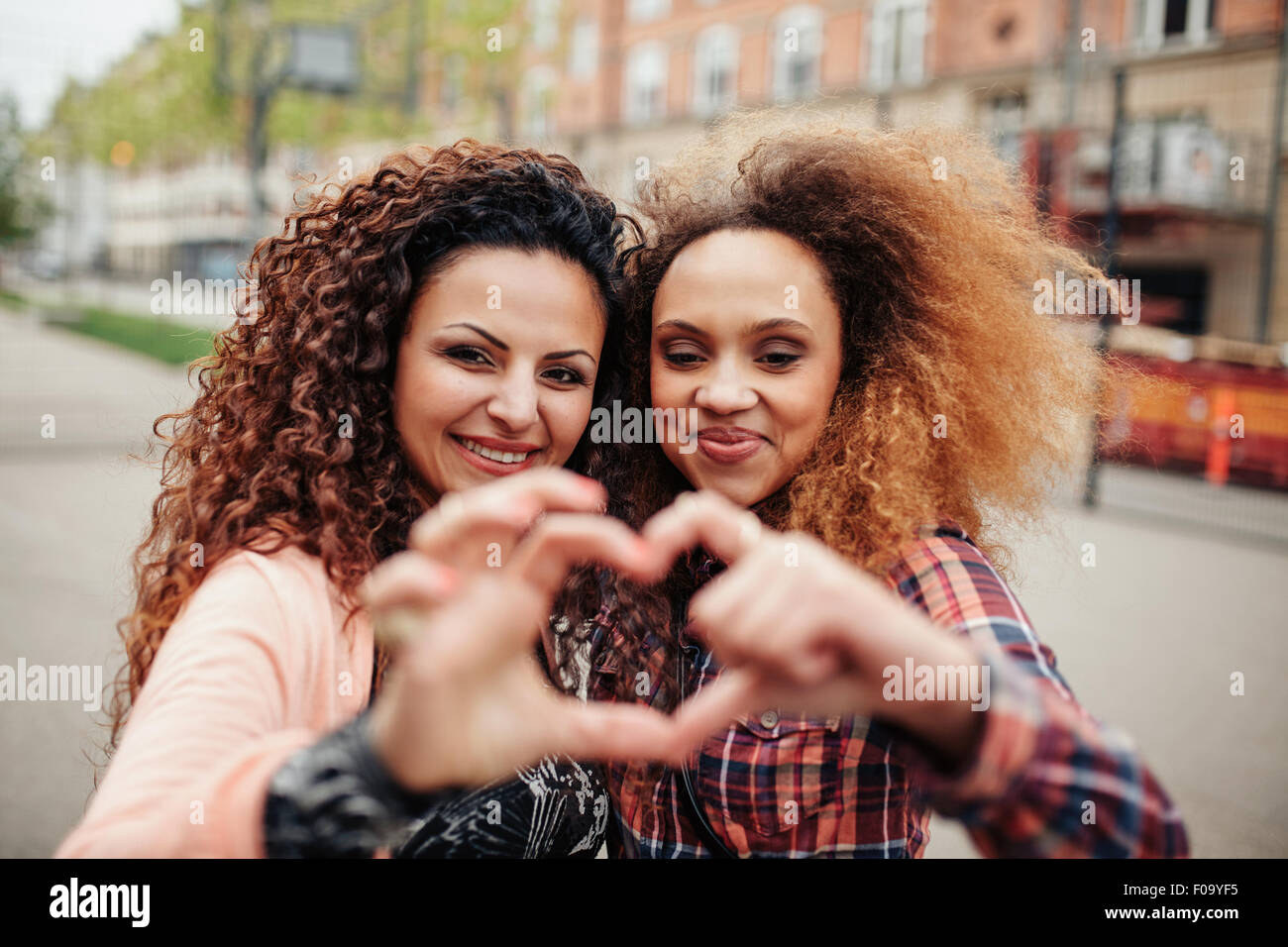 Bella giovane donna messa a forma di cuore con le dita. Due donne in piedi insieme all'aperto sulla strada della citta'. Foto Stock