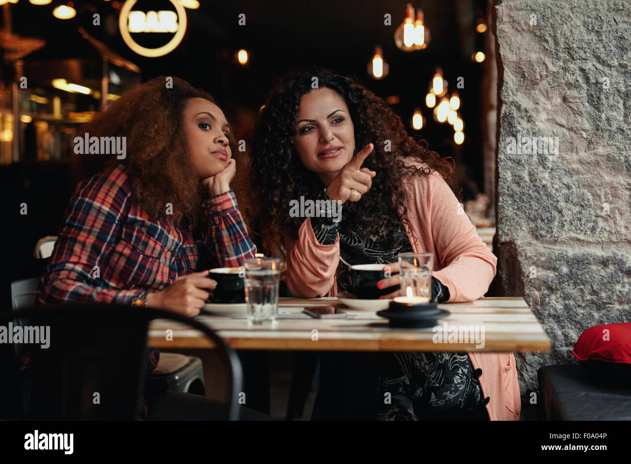 Due giovani donne seduti ad un ristorante che guarda lontano con una punta lontano mostrando qualcosa al suo amico. Foto Stock