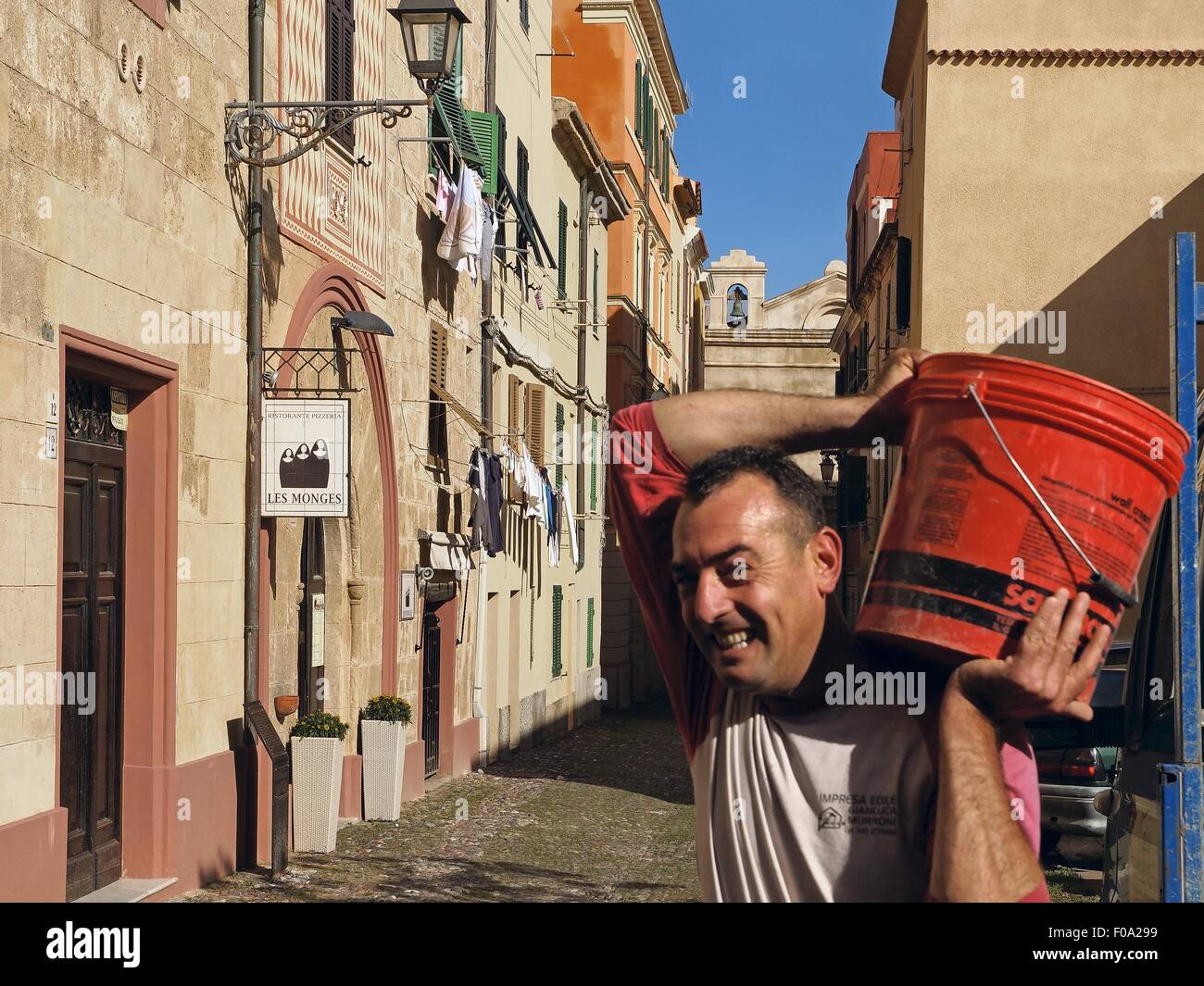 Uomo che porta secchio di vernice e camminare sul vicolo della città vecchia in Sardegna, Italia Foto Stock