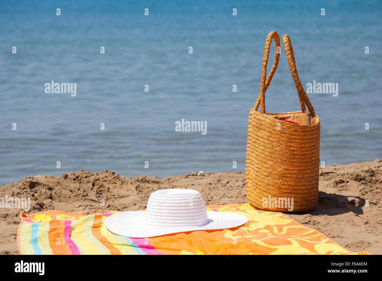 Diversi accessori per la spiaggia, borsa hat e colori Asciugamano messo sulla sabbia vicino al mare di acqua. Essa è al centro di un soleggiato d estate Foto Stock