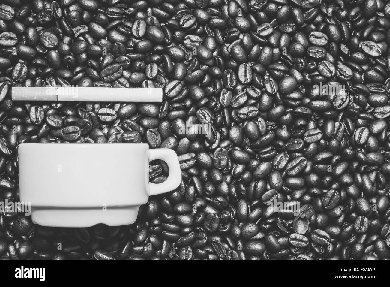 Tazza di caffè accanto a una sigaretta sulla sommità del caffè in grani Foto Stock