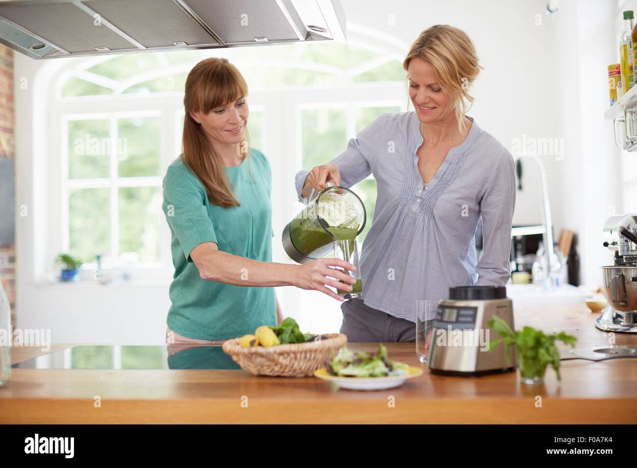 Le donne di bere verde frullato vegano in cucina Foto Stock