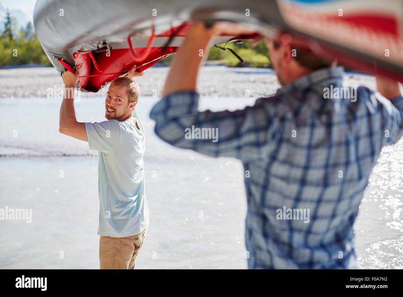 Vista posteriore di due uomini che trasportano dinghy sopra le loro teste ad acqua Foto Stock