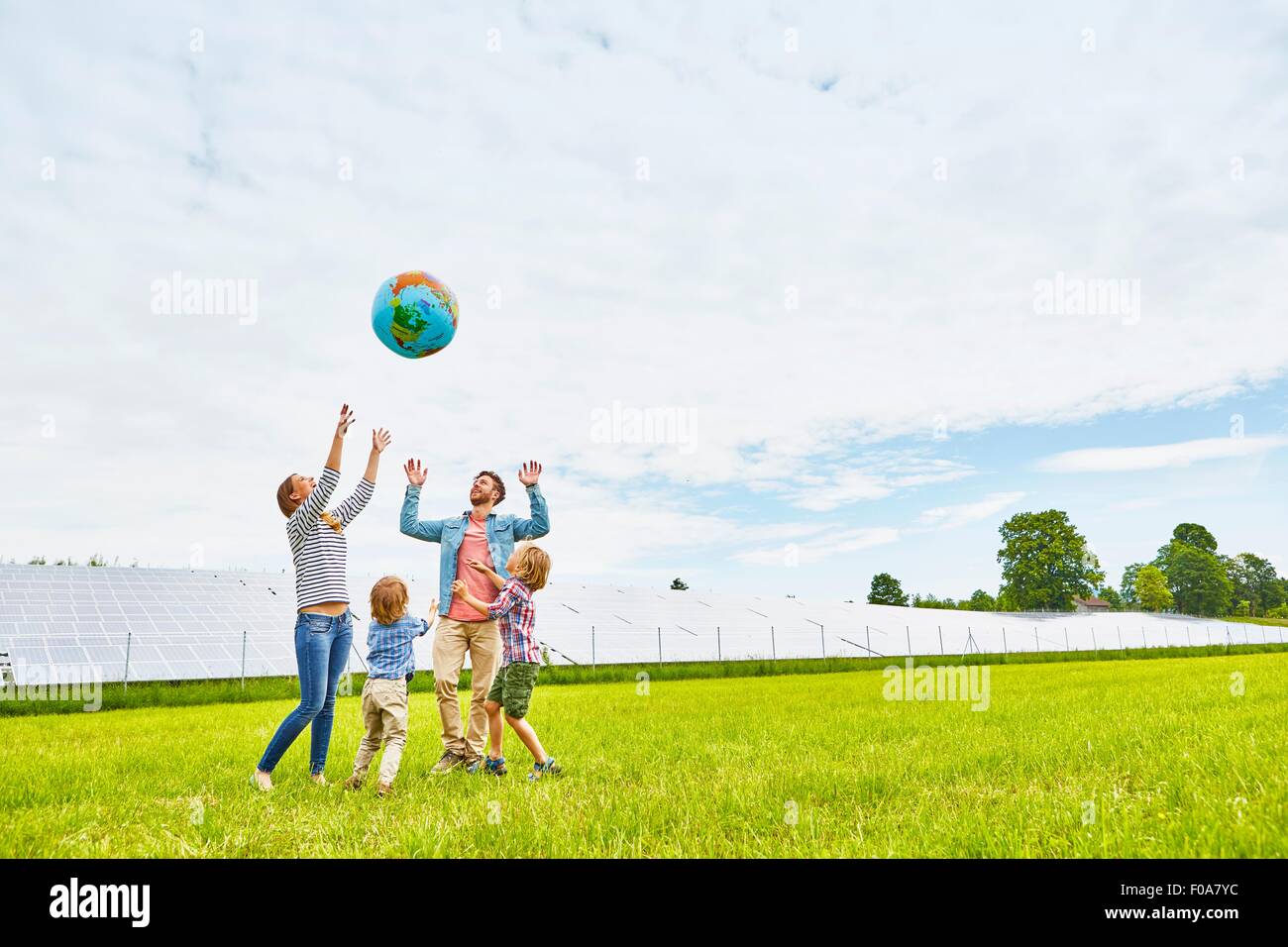 Famiglia giovane giocando con il pallone gonfiabile, sul campo, accanto alla fattoria solare Foto Stock