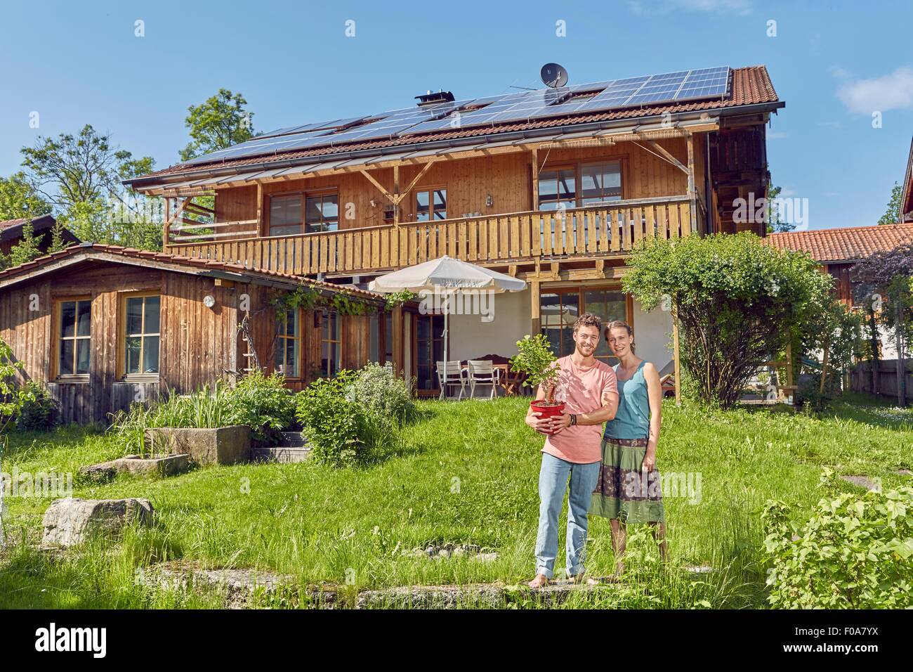 Ritratto di giovane coppia, azienda impianto pot, in piedi di fronte a casa con pannelli solari sul tetto Foto Stock